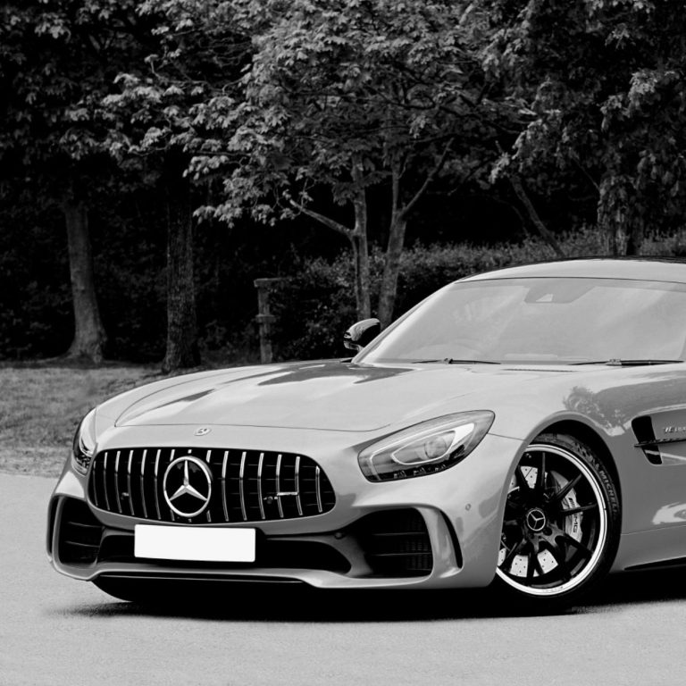 Luxus Auto Silberner Mercedes AMG GT mit sportlichem Design, geparkt vor Bäumen.